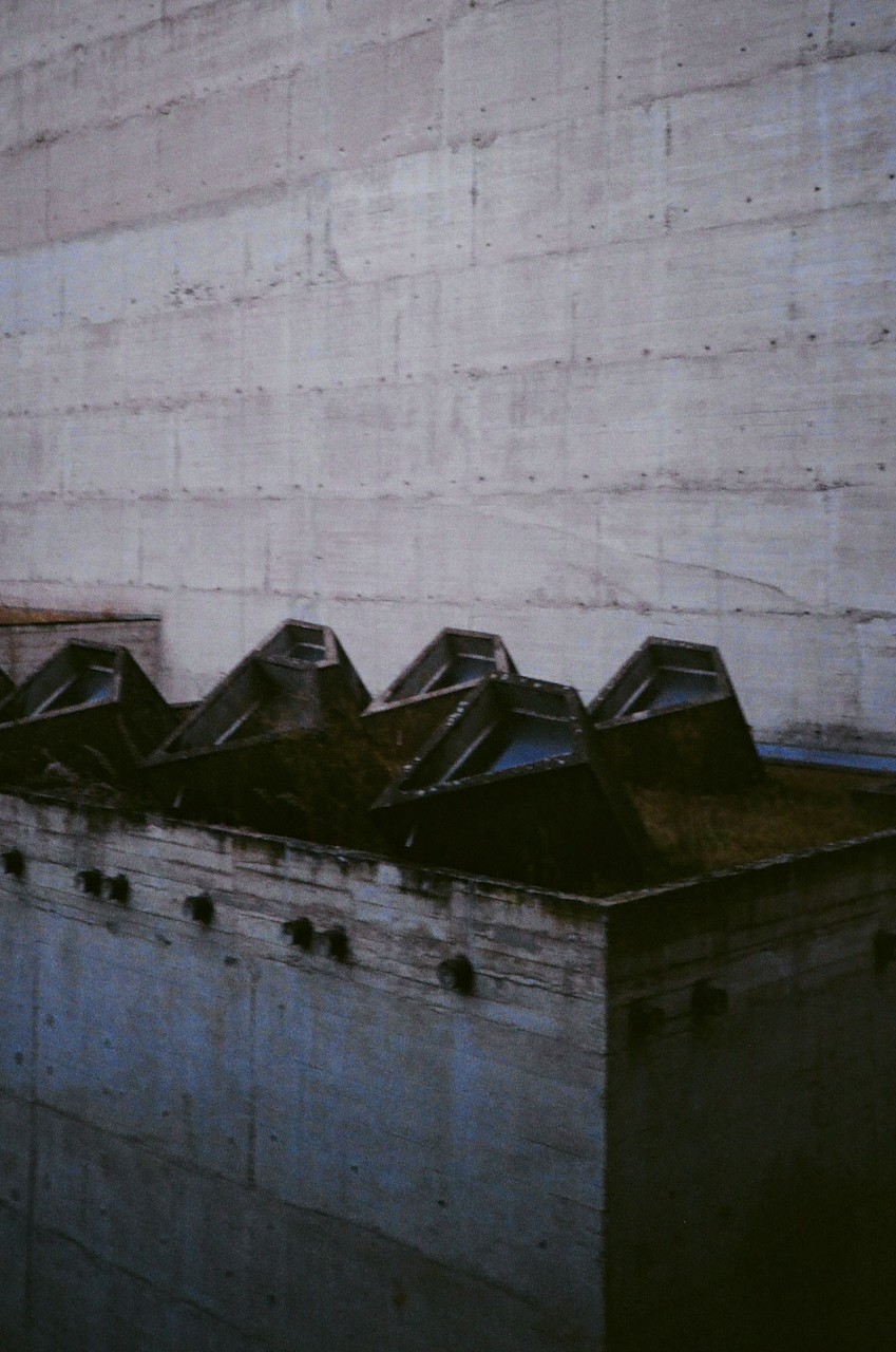 A tall, gray building with a large, empty space on the ground floor