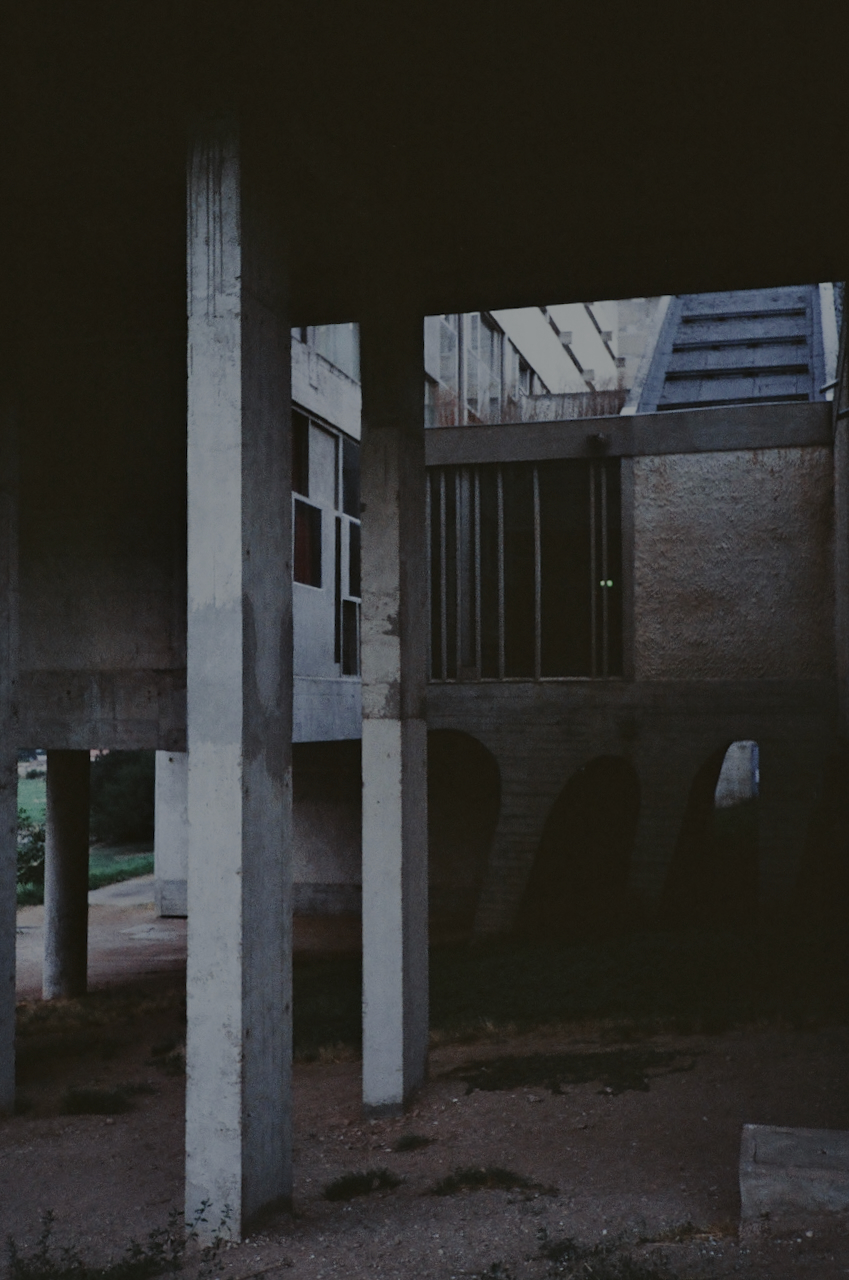 This is a black and white photograph of an abandoned building with a large, open structure in the foreground. The building has a rusted appearance and is surrounded by a barren landscape