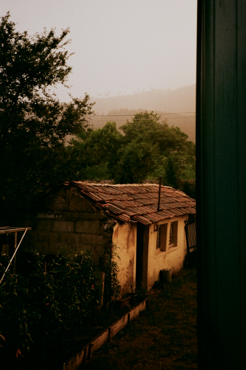 A house with a slanted roof in a rural setting, viewed through a window