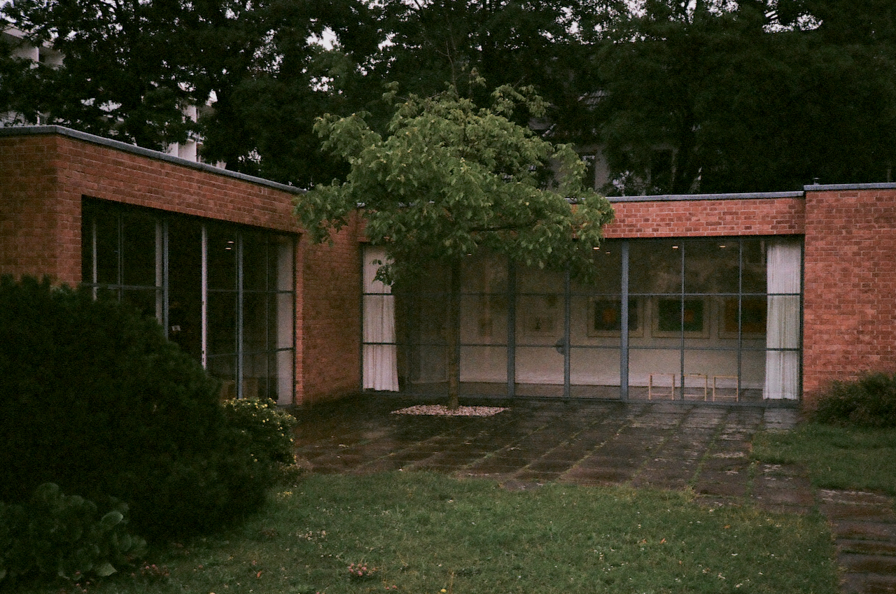A brick building with a glass front door, surrounded by a paved area and trees