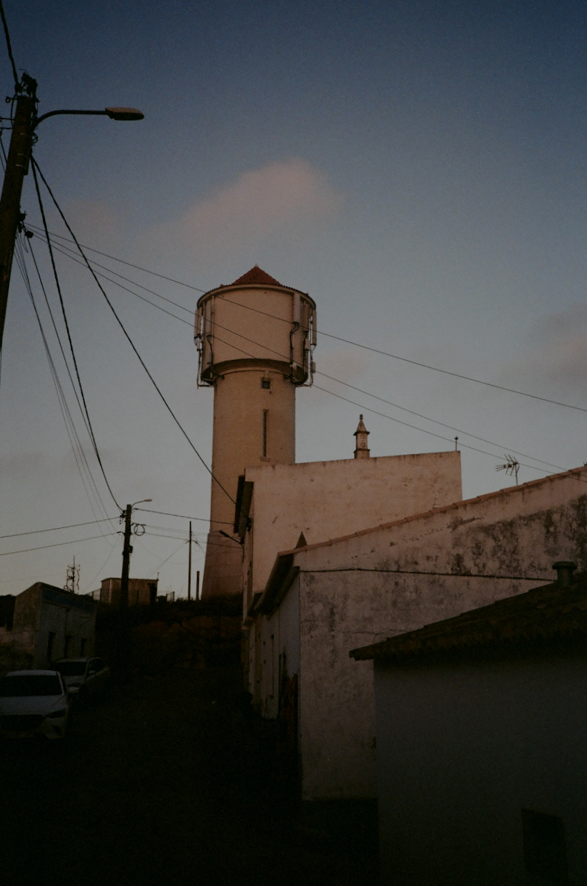 A white tower with a red roof stands next to a building in a rural setting