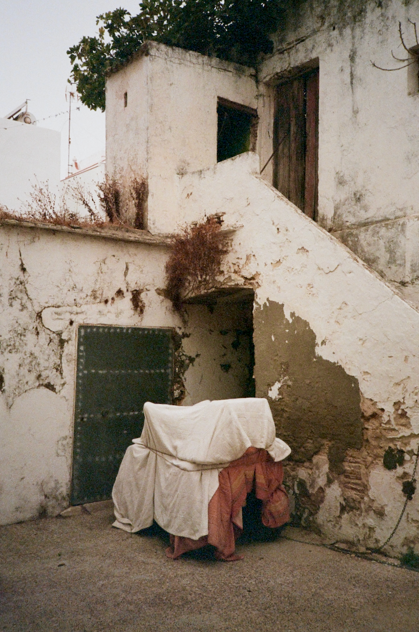A dilapidated building with a staircase, a covered area, and a small table