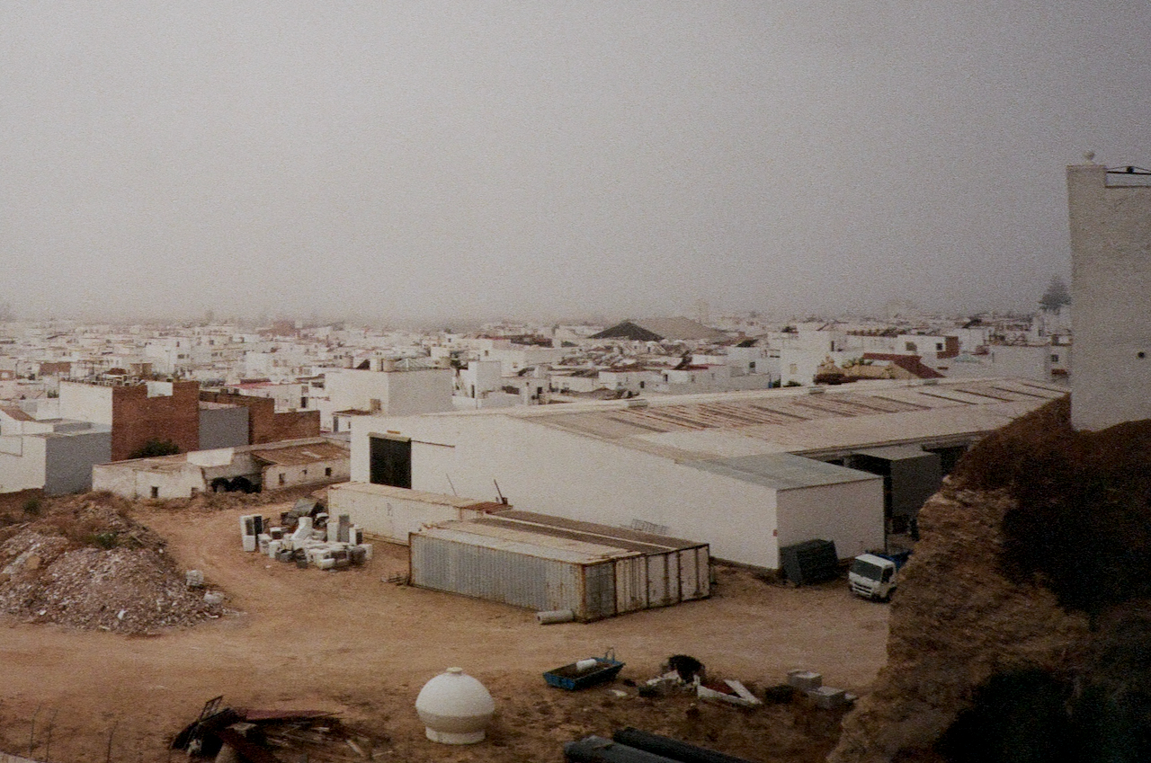 Aerial view of a barren, industrial area with buildings, vehicles, and a hazy sky