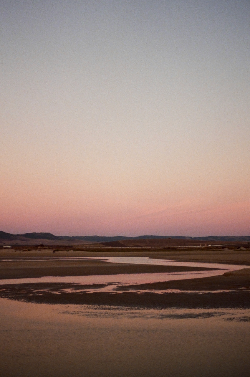A tranquil scene of a sunset over a body of water, with a clear sky and a calm atmosphere