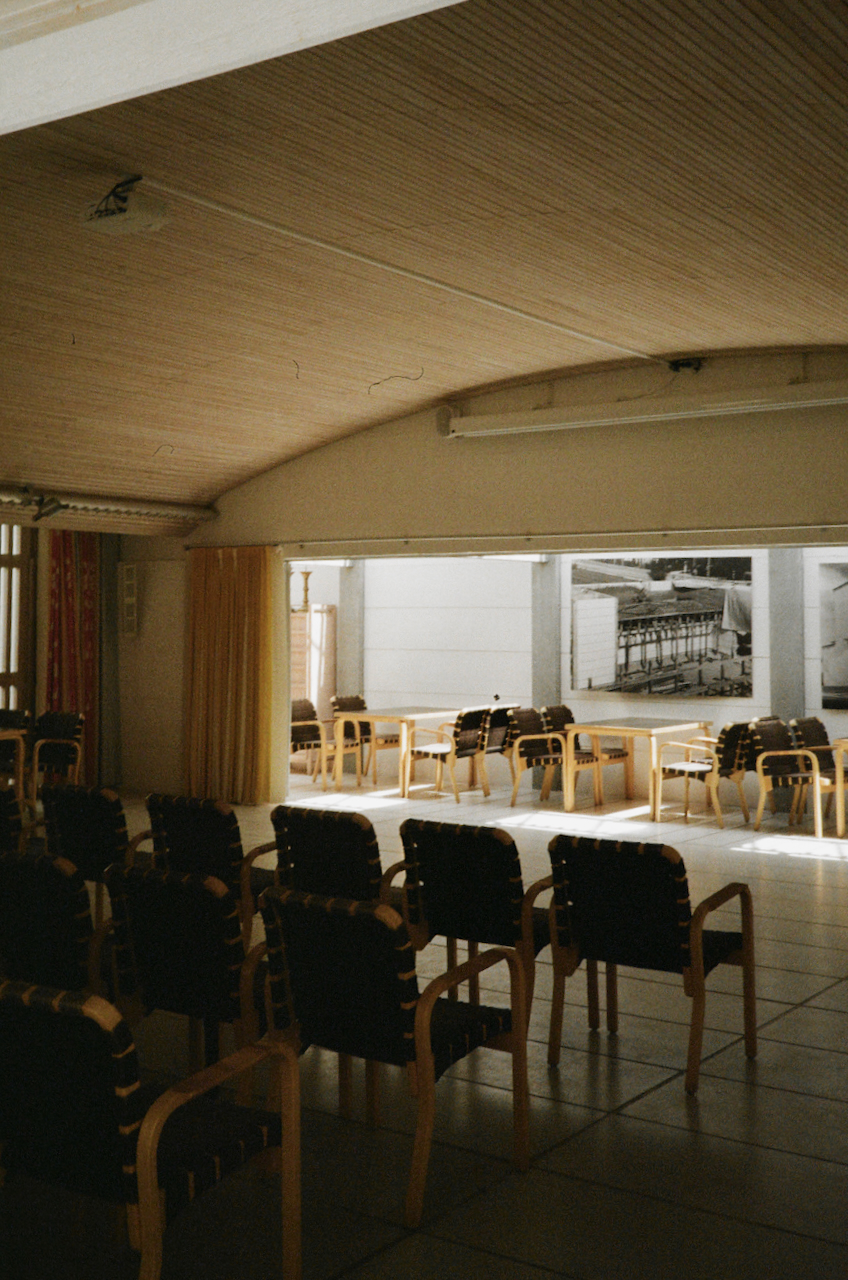 A large, empty room with rows of chairs facing a stage or front of the room, and a high ceiling with exposed rafters